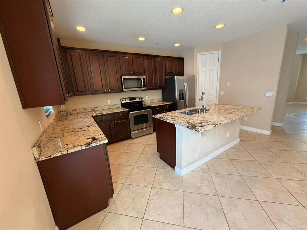 A kitchen features dark wood cabinets, granite countertops, stainless steel appliances, and tile flooring — 1162 BOLTON PLACE, LAKE MARY, FL