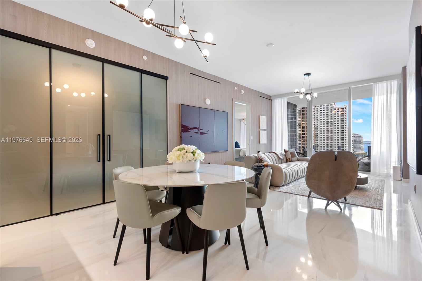 A modern dining and living area features a round marble table, glass partitions, and city views — 300 Biscayne Blvd Way # 1605, Miami FL 33131, MIAMI, FL
