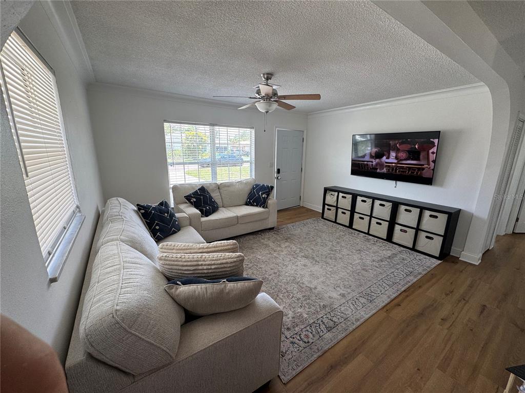 A living room features a light-colored sectional sofa, a loveseat, a rug, and a wall-mounted television — 631 75TH AVENUE N, ST PETERSBURG, FL