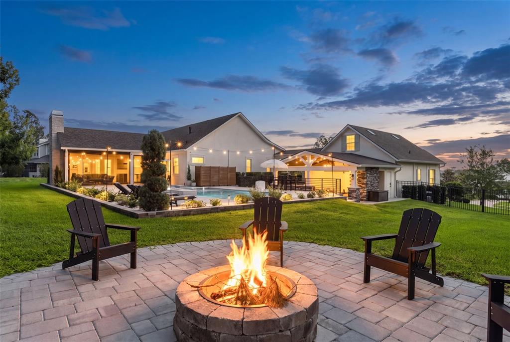 A backyard fire pit with Adirondack chairs overlooks a swimming pool and a residential house — 20085 ENGLISH WALNUT PLACE, BROOKSVILLE, FL