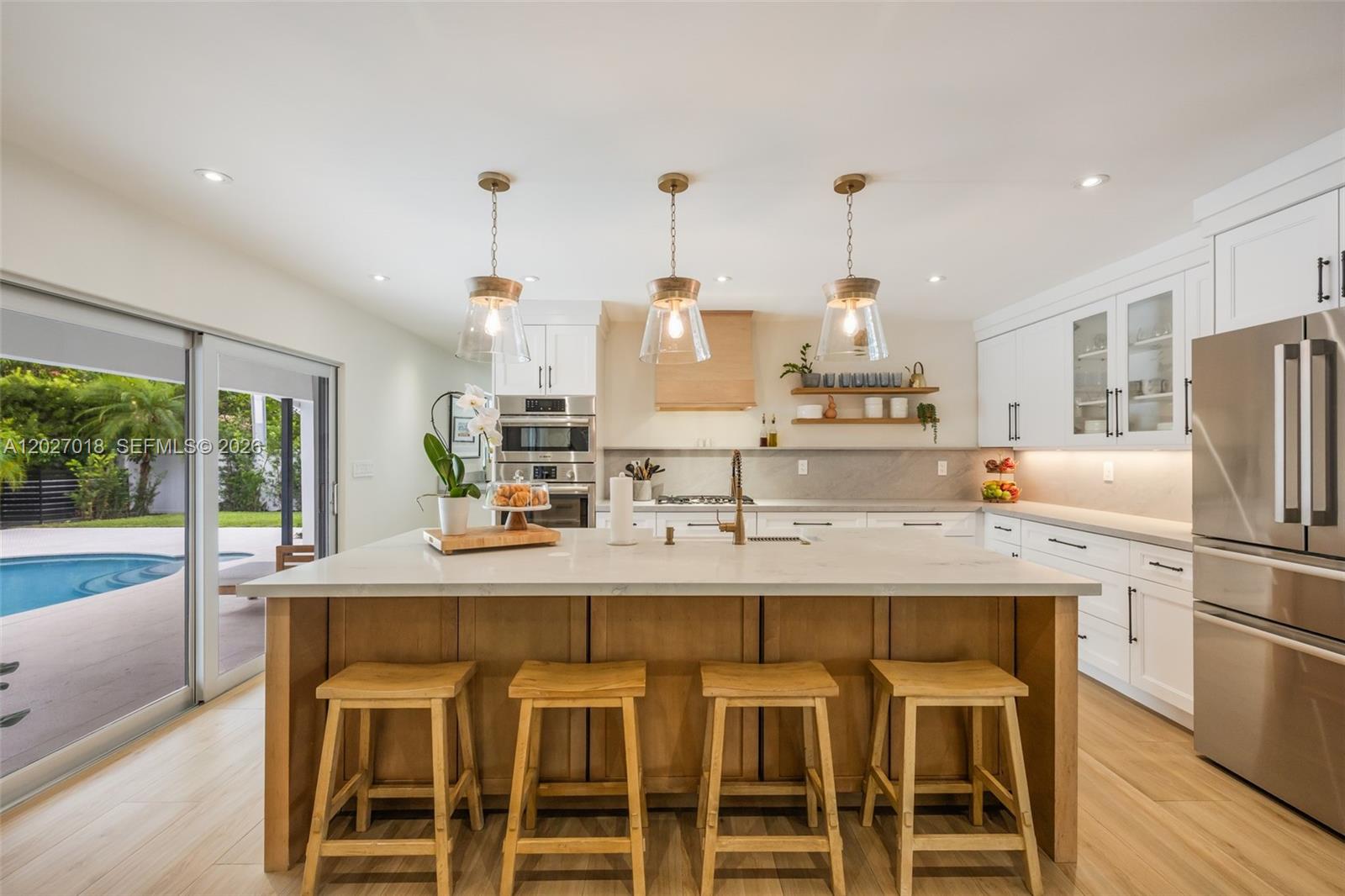 A modern kitchen features a wooden island with bar stools, white cabinetry, and stainless appliances — 4730 SW 89th Ave, Miami FL 33165, MIAMI, FL