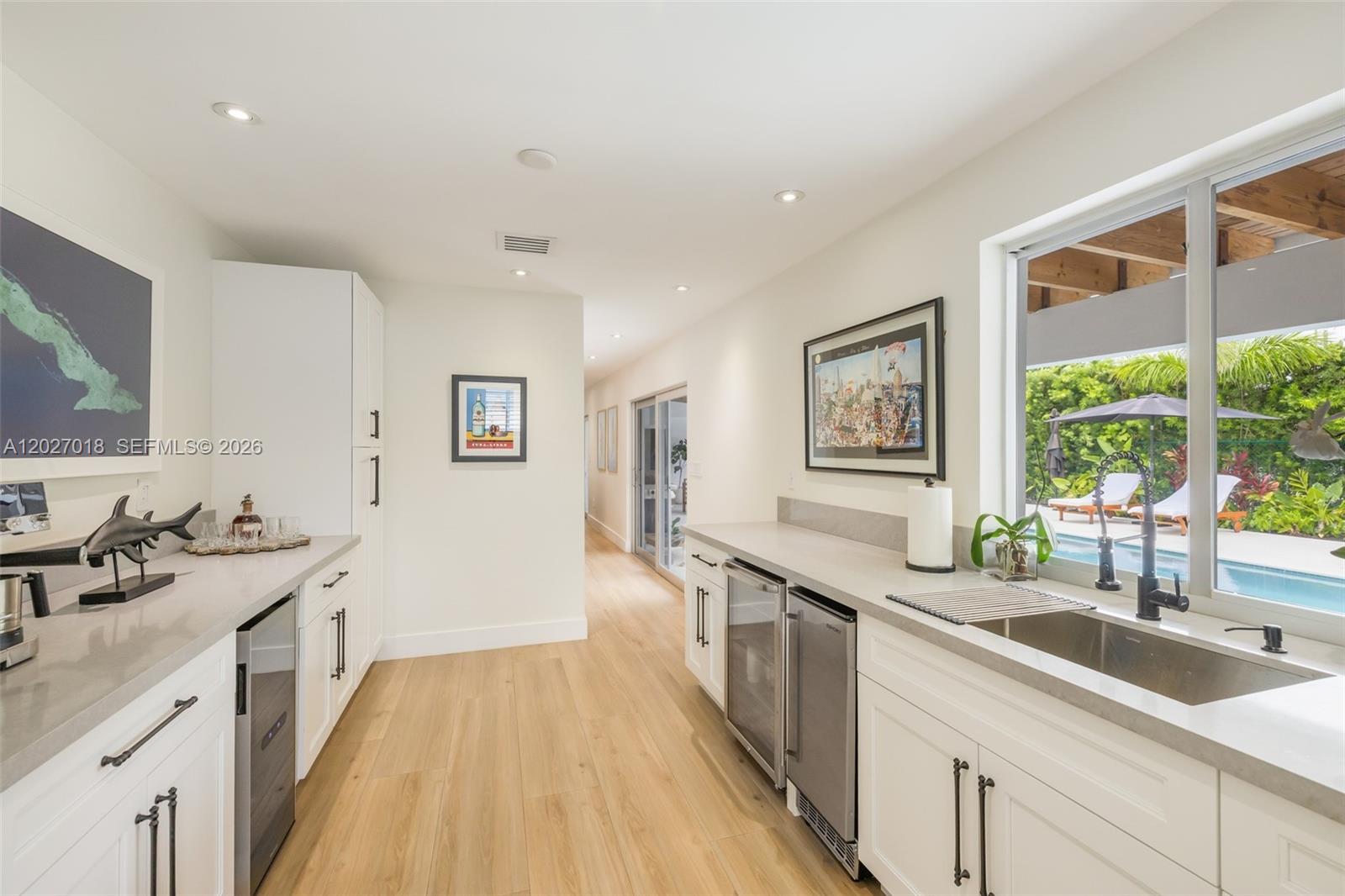 A modern kitchen features white cabinetry, light wood floors, and a view of a pool — 4730 SW 89th Ave, Miami FL 33165, MIAMI, FL