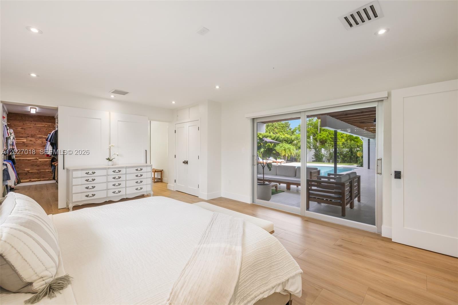 A bedroom features white walls, light wood flooring, a dresser, and sliding doors to a pool — 4730 SW 89th Ave, Miami FL 33165, MIAMI, FL