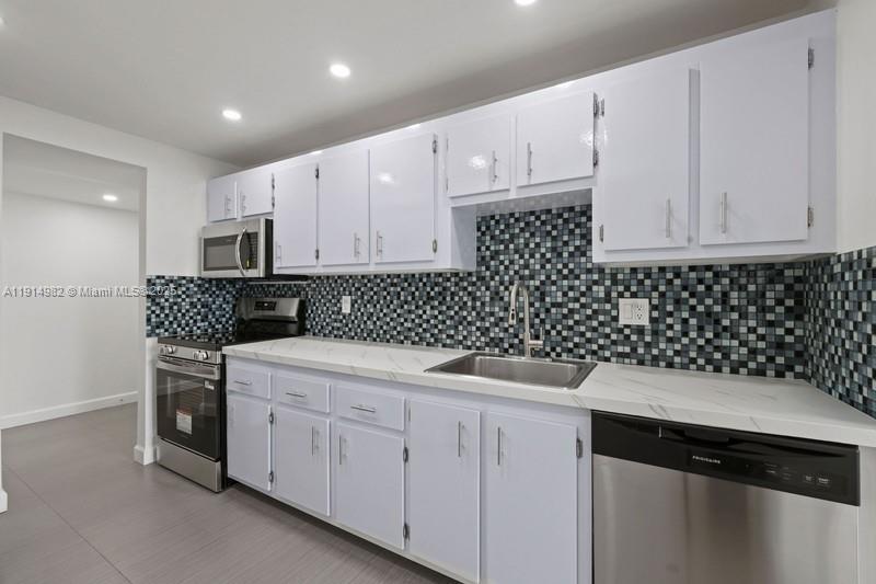 A kitchen features white cabinets, a mosaic tile backsplash, stainless steel appliances, and marble-look countertops — 4174 Inverrary Dr # 902, Lauderhill FL 33319, LAUDERHILL, FL