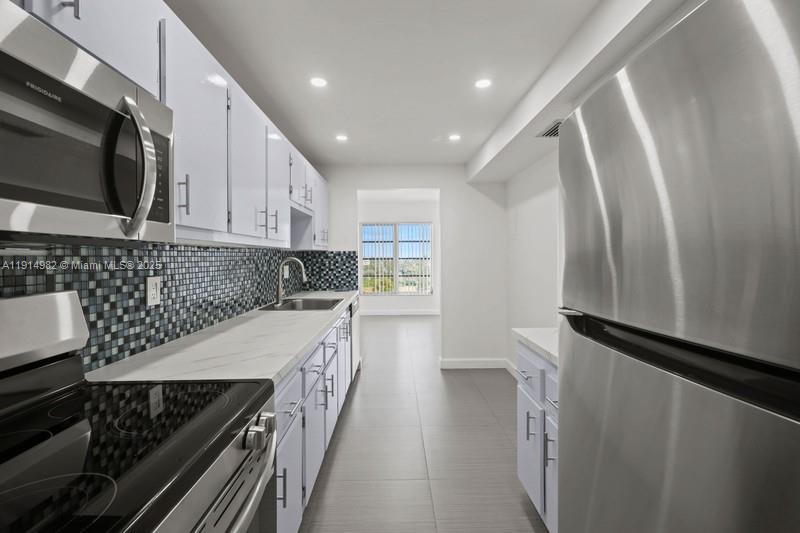 A galley kitchen features white cabinets, stainless steel appliances, and a blue mosaic tile backsplash — 4174 Inverrary Dr # 902, Lauderhill FL 33319, LAUDERHILL, FL