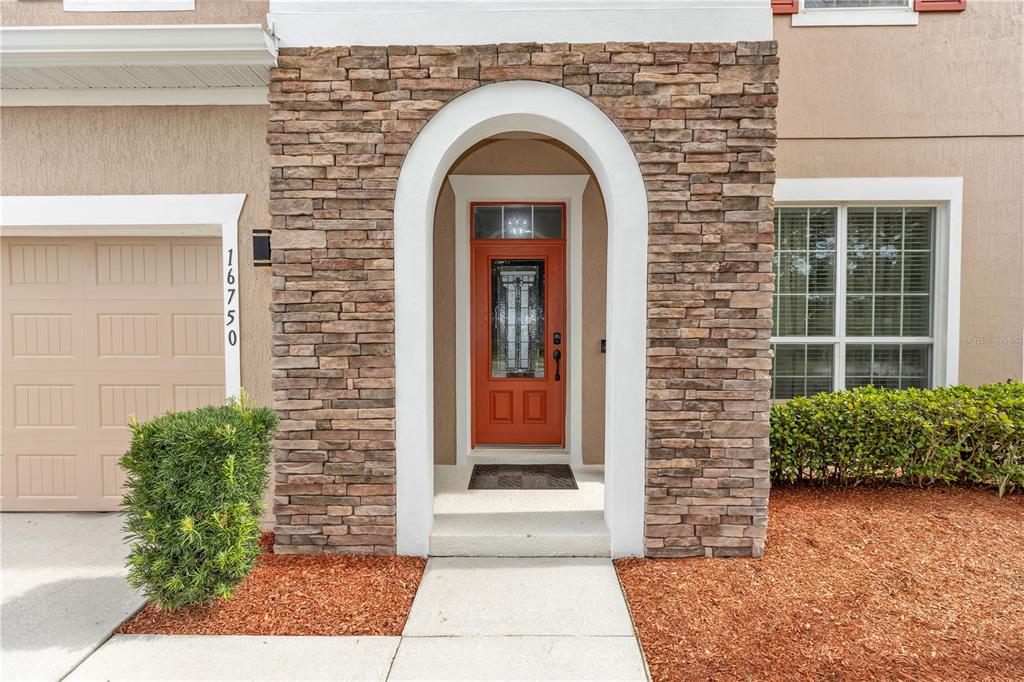 The exterior view shows a house entrance with a stone-faced archway and orange front door — 16750 ABBEY HILL COURT, CLERMONT, FL