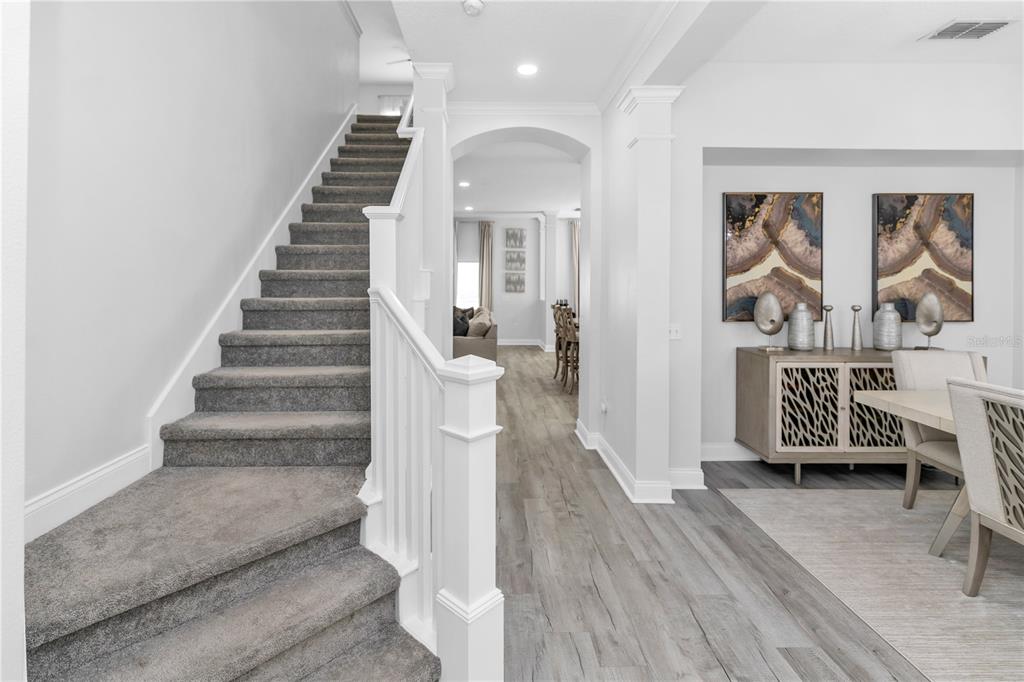 A carpeted staircase leads upstairs next to a dining area with wood-look flooring — 16750 ABBEY HILL COURT, CLERMONT, FL