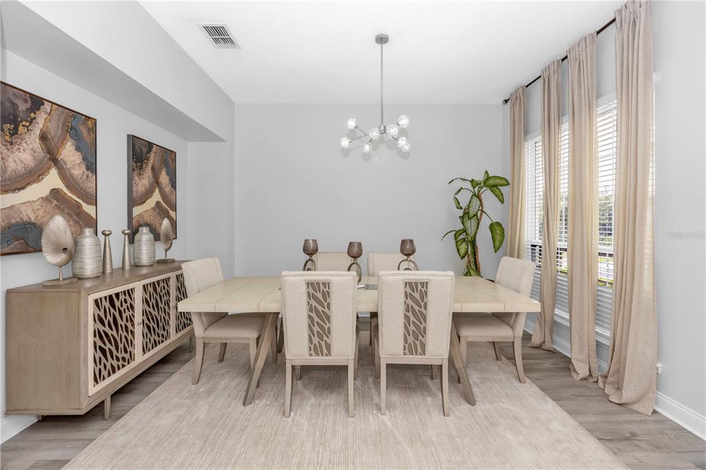 A dining room features a light-colored table, upholstered chairs, a sideboard, and a modern chandelier — 16750 ABBEY HILL COURT, CLERMONT, FL