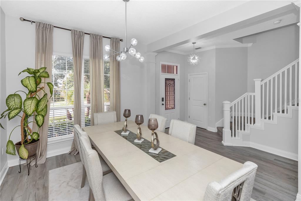 A dining room features a long table, modern chandelier, large windows, and a staircase — 16750 ABBEY HILL COURT, CLERMONT, FL