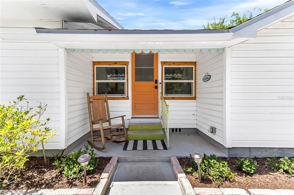 A white-sided house exterior features a bright orange front door and a wooden rocking chair — 3560 MARTIN AVENUE, MOUNT DORA, FL