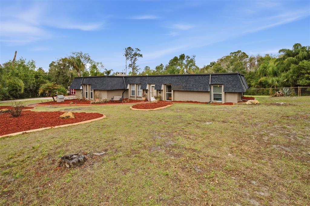 A single-story house with a dark mansard roof sits on a grassy lot with landscaping — 7815 TANGLEWOOD DRIVE, NEW PORT RICHEY, FL