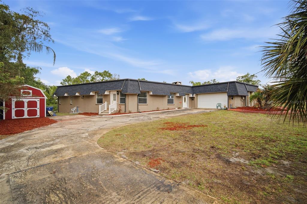 A single-story house with a dark mansard roof, beige stucco exterior, and a red shed — 7815 TANGLEWOOD DRIVE, NEW PORT RICHEY, FL