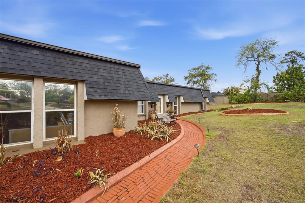 A brick walkway curves along the side of a house with a dark shingled roof — 7815 TANGLEWOOD DRIVE, NEW PORT RICHEY, FL