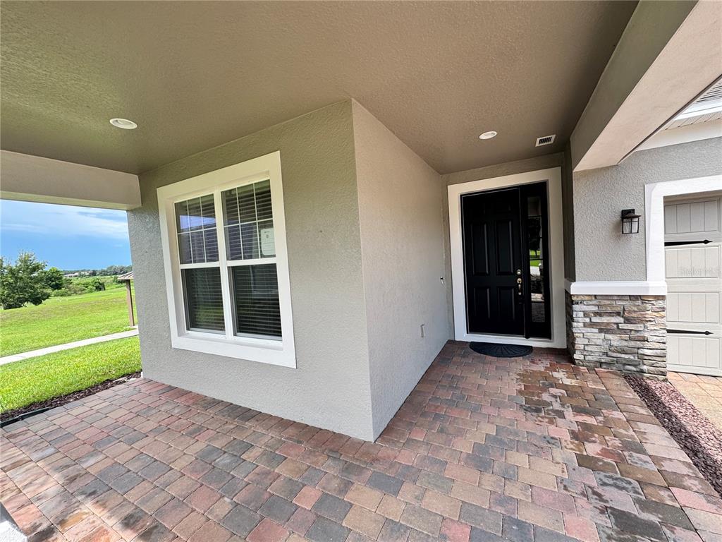 A covered entryway features a paver floor, a black front door, and stone siding accents — 31936 GEOFF WAY, SORRENTO, FL