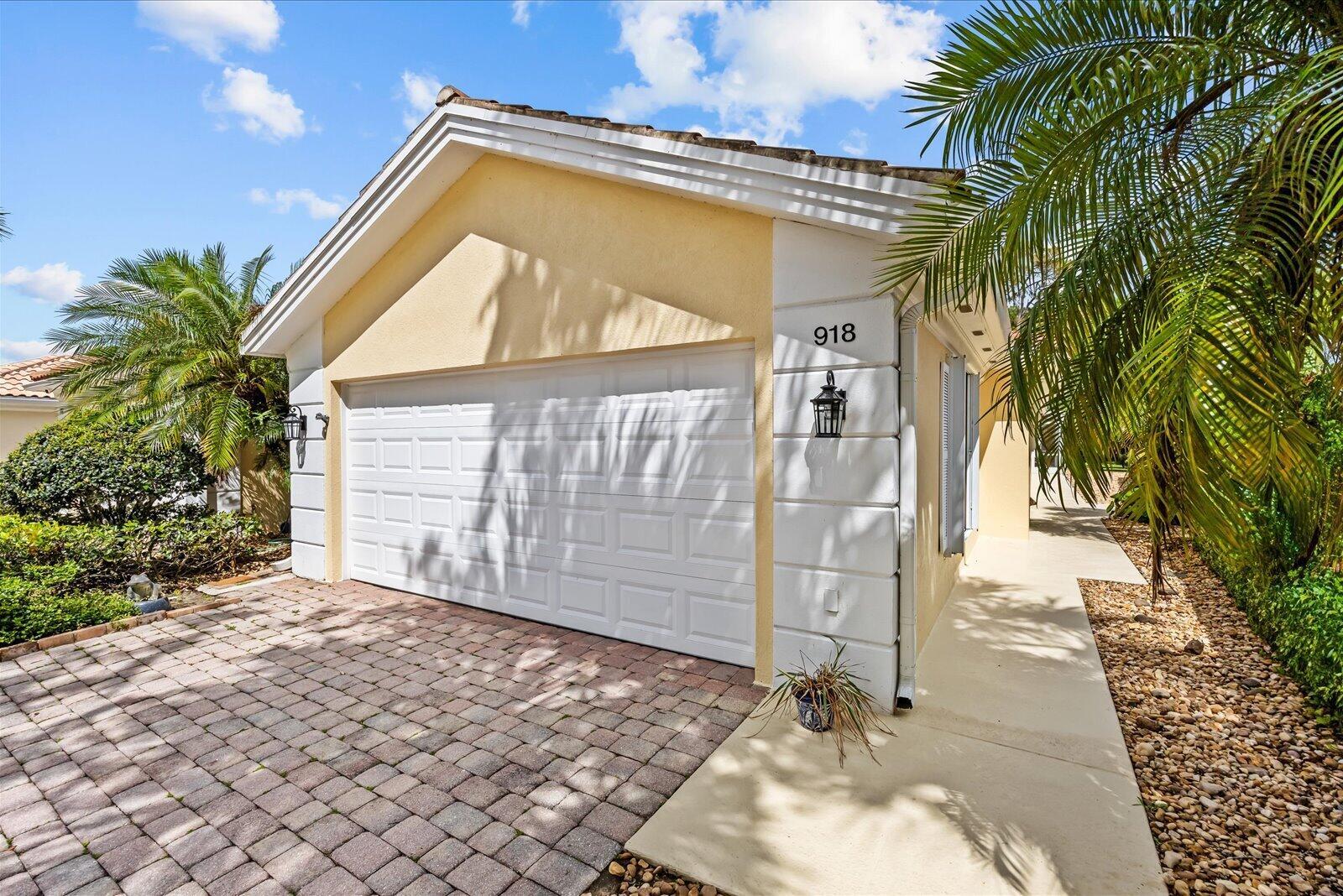 A beige house exterior features a white garage door, a brick driveway, and palm trees — 918 SW Balmoral Trace, Stuart FL 34997, STUART, FL