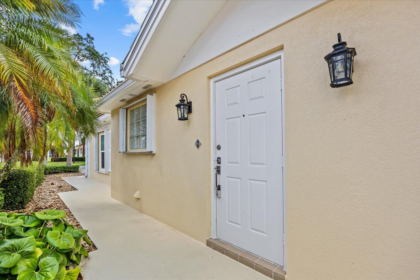 A white front door is centered on the beige exterior wall of a residential home — 918 SW Balmoral Trace, Stuart FL 34997, STUART, FL