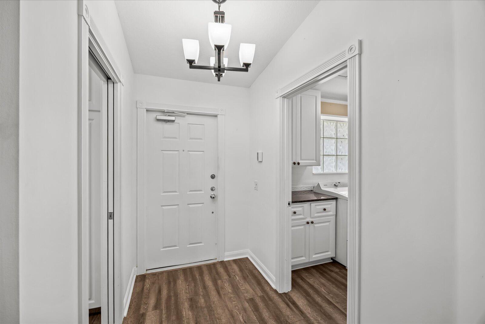 A white front door opens into a small foyer with wood-look flooring and a chandelier — 918 SW Balmoral Trace, Stuart FL 34997, STUART, FL