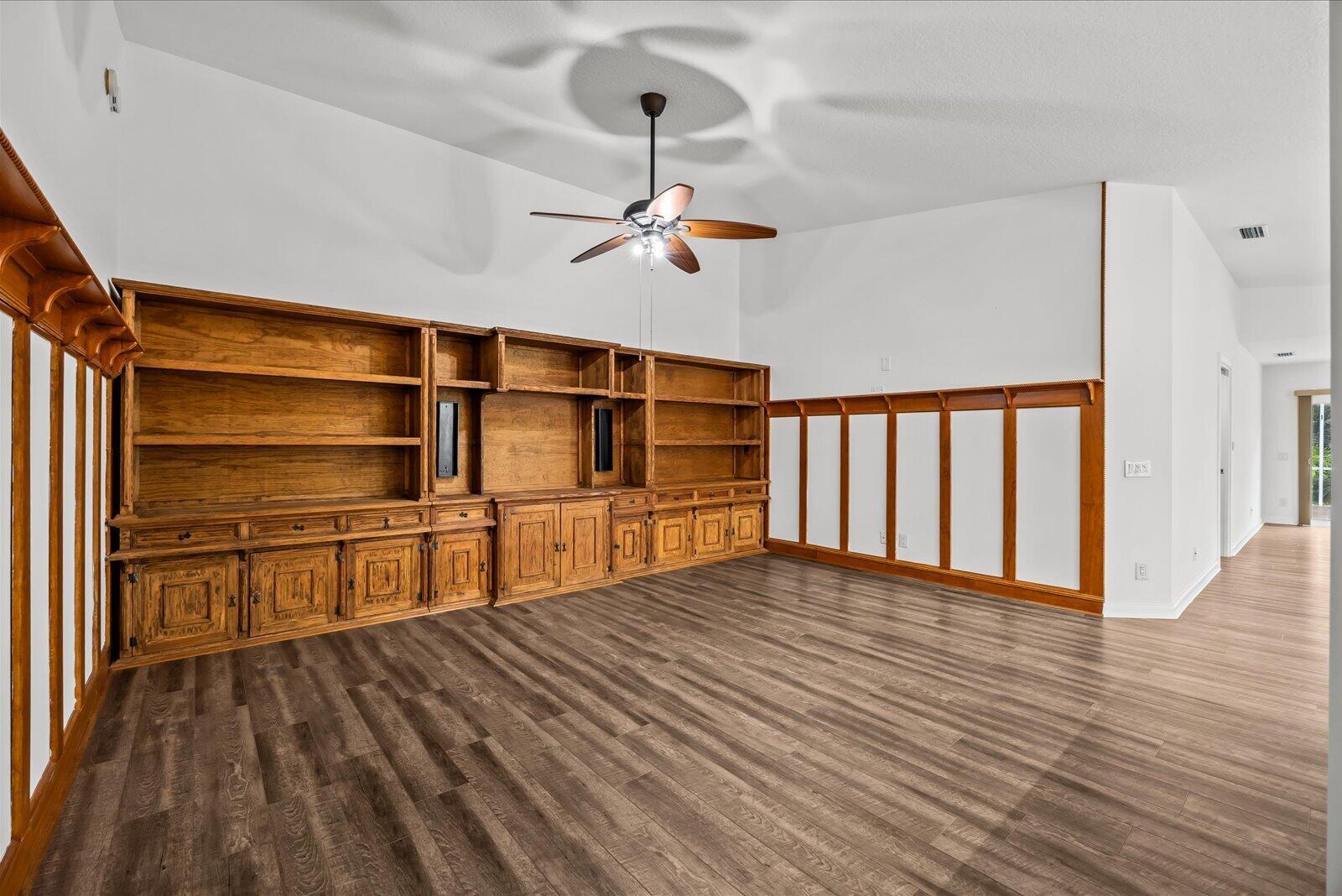 A room with wood-look flooring, built-in wooden shelving, and wall paneling under a vaulted ceiling — 918 SW Balmoral Trace, Stuart FL 34997, STUART, FL