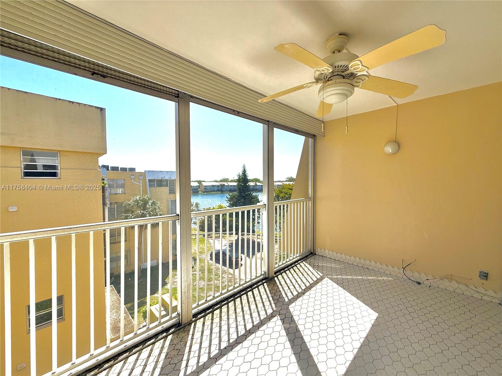 A screened-in balcony features a ceiling fan, tiled flooring, and views of a nearby lake — 920 NE 199th St # 4J, Miami FL 33179, MIAMI, FL