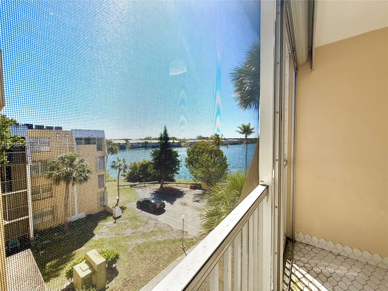 A view of a lake and parking lot from a screened-in balcony — 920 NE 199th St # 4J, Miami FL 33179, MIAMI, FL