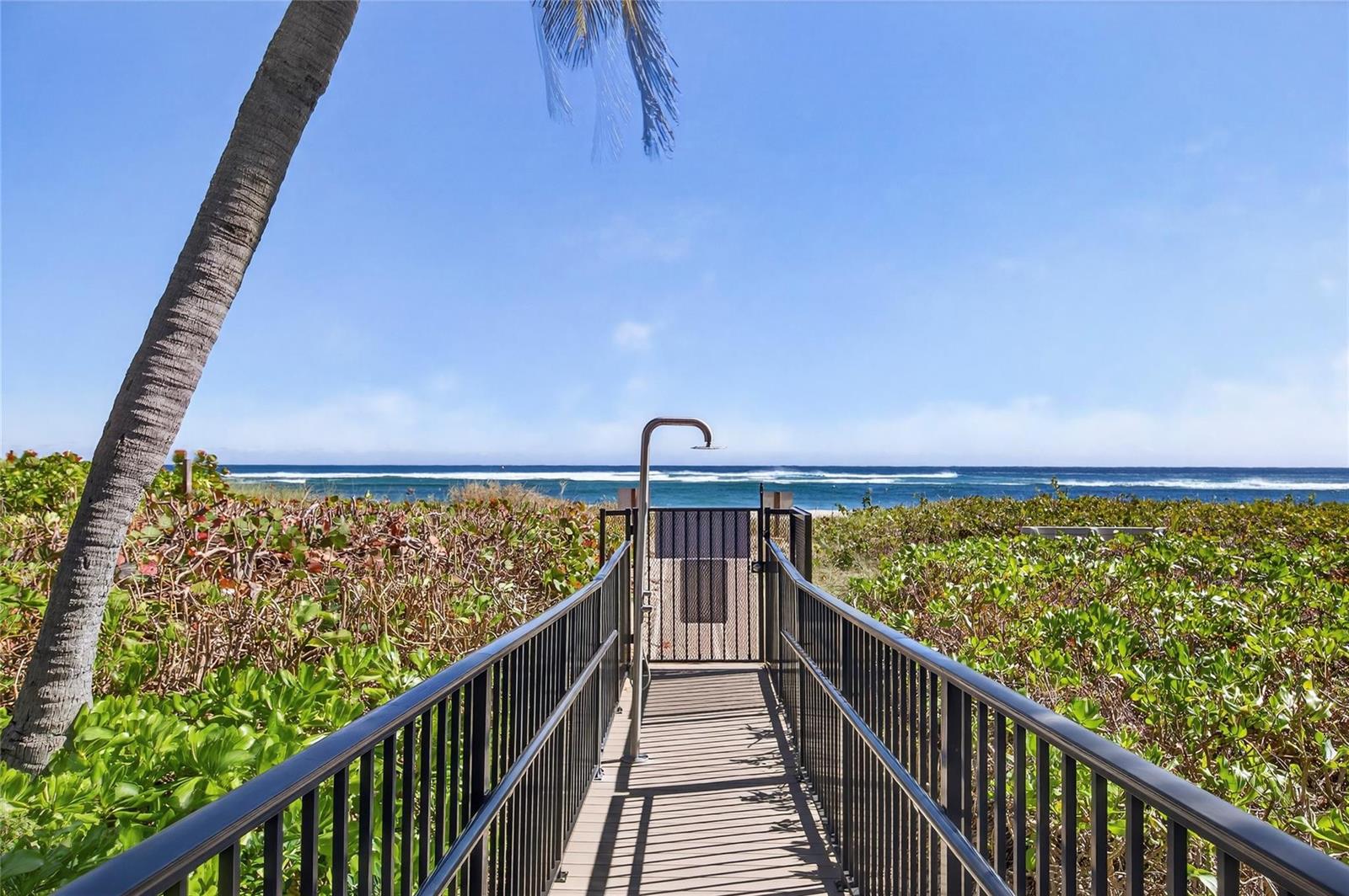 A metal walkway leads through lush greenery to a beach access gate with an outdoor shower — 1500 N Ocean Boulevard # 203, Pompano Beach FL 33062, POMPANO BEACH, FL