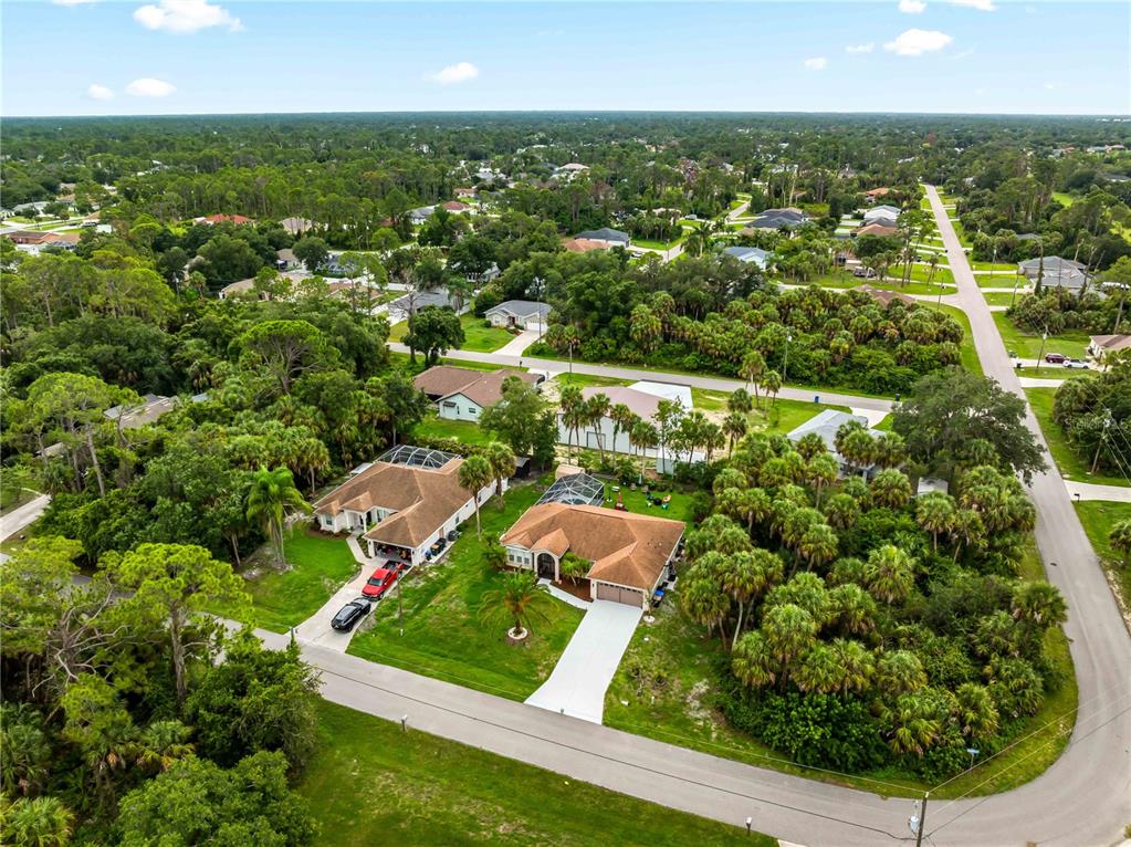 An aerial view shows two suburban houses surrounded by dense trees and a paved road — 4243 FONSICA AVENUE, NORTH PORT, FL
