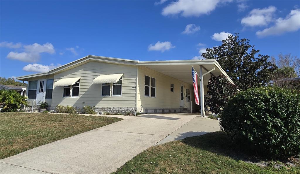 A light yellow manufactured home features a concrete driveway, a carport, and an American flag — 3450 N CITRUS CIRCLE UNIT GE, ZELLWOOD, FL