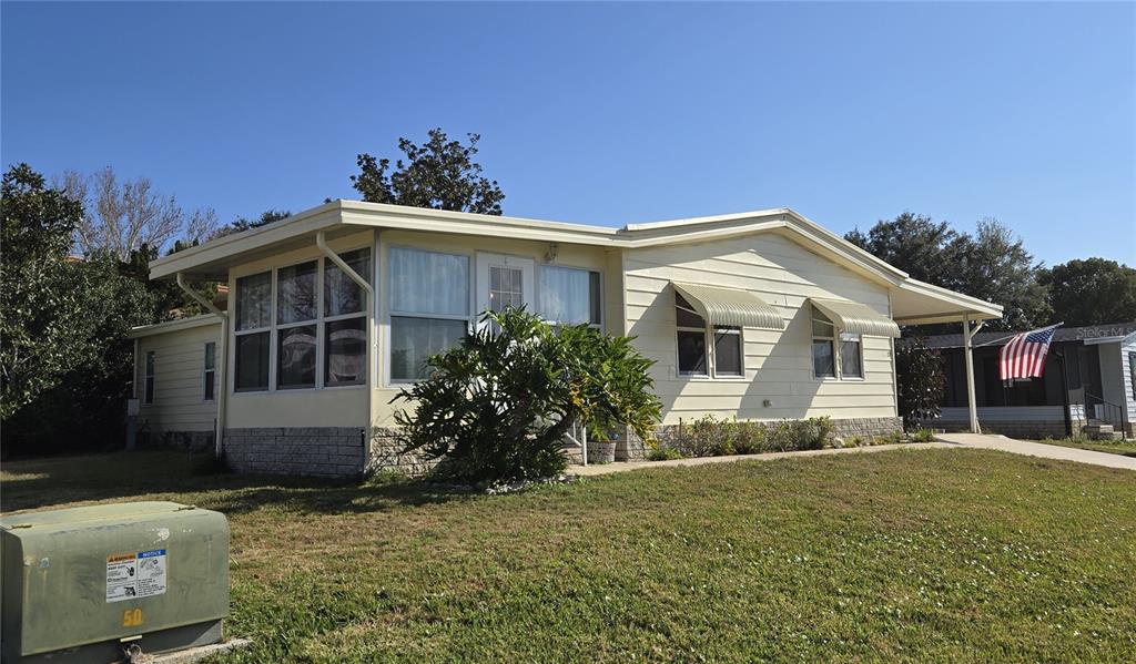 A light yellow manufactured home with a sunroom and a carport under a clear sky — 3450 N CITRUS CIRCLE UNIT GE, ZELLWOOD, FL