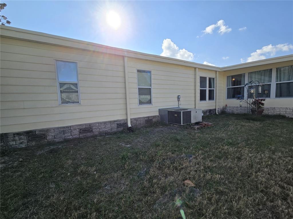 The exterior of a light yellow manufactured home with a brick-patterned skirting and AC unit — 3450 N CITRUS CIRCLE UNIT GE, ZELLWOOD, FL