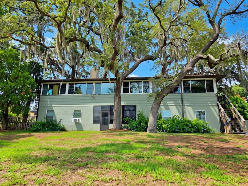 A two-story green house with large windows and mature trees in the front yard — 10844 POINCIANA DRIVE, CLERMONT, FL