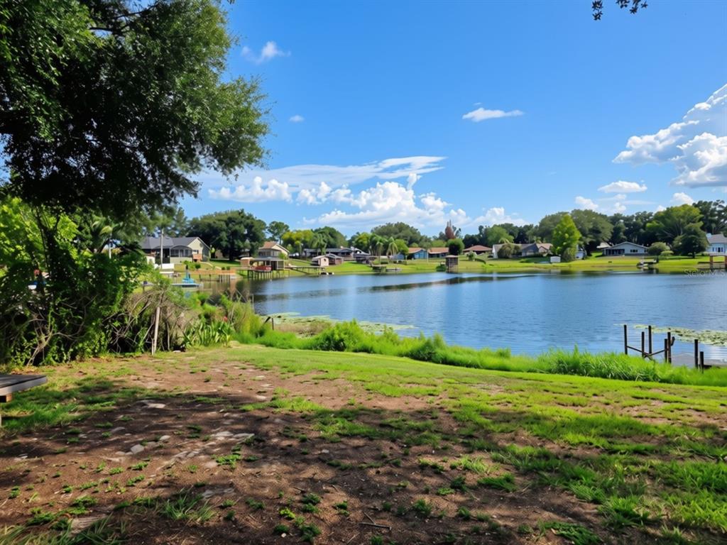 A grassy yard overlooks a lake with houses and boat docks along the distant shore — 10844 POINCIANA DRIVE, CLERMONT, FL
