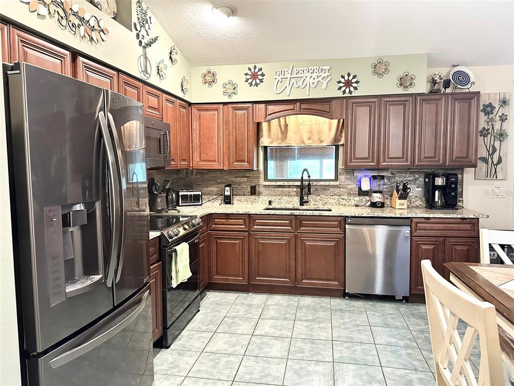A kitchen features dark wood cabinets, stainless steel appliances, granite countertops, and tile flooring — 10844 POINCIANA DRIVE, CLERMONT, FL