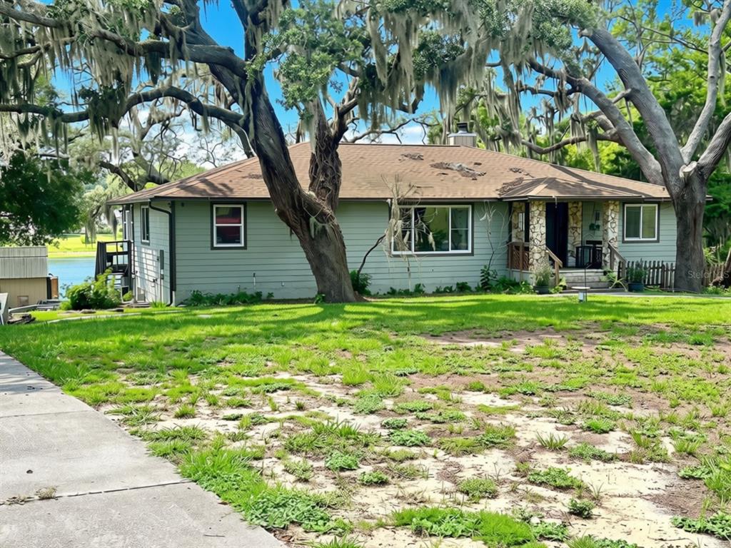 A light green house with a brown roof sits on a grassy lot with large trees — 10844 POINCIANA DRIVE, CLERMONT, FL