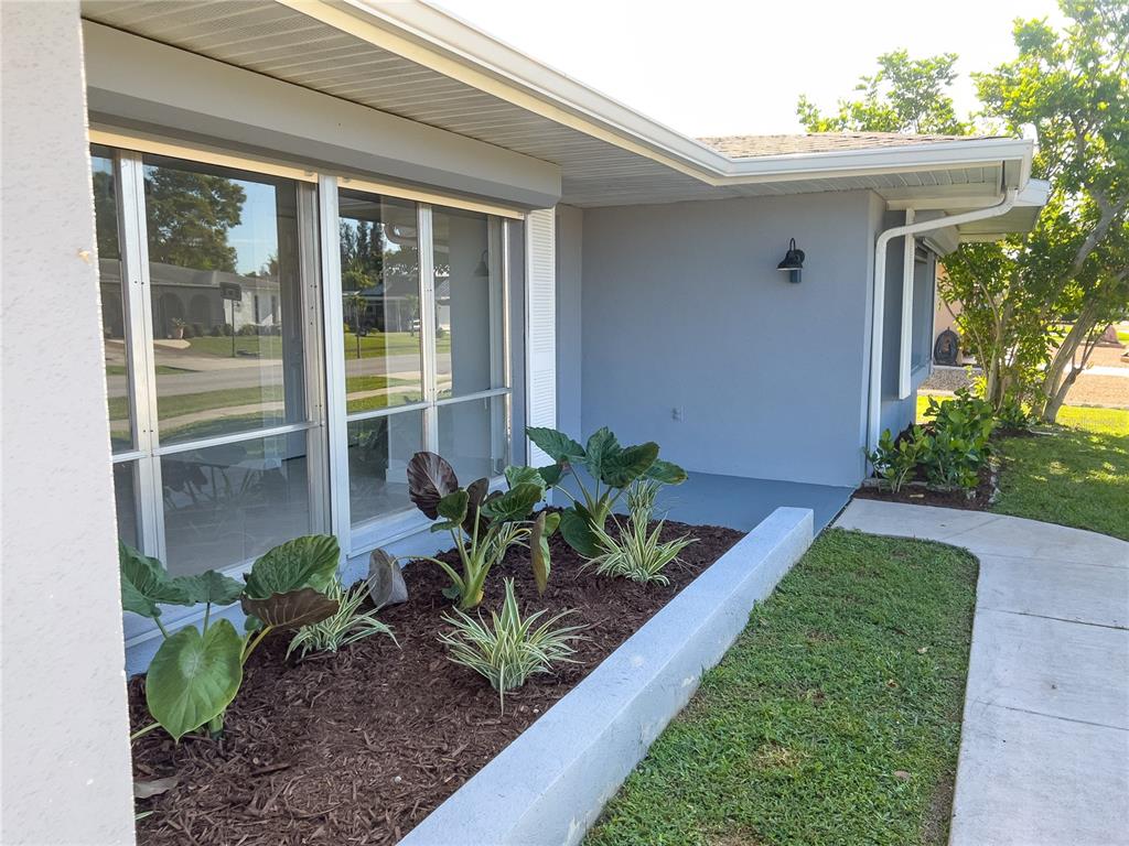 A gray house exterior features a landscaped garden bed with large-leaf plants and mulch — 326 WHERLEY AVENUE SE, PORT CHARLOTTE, FL