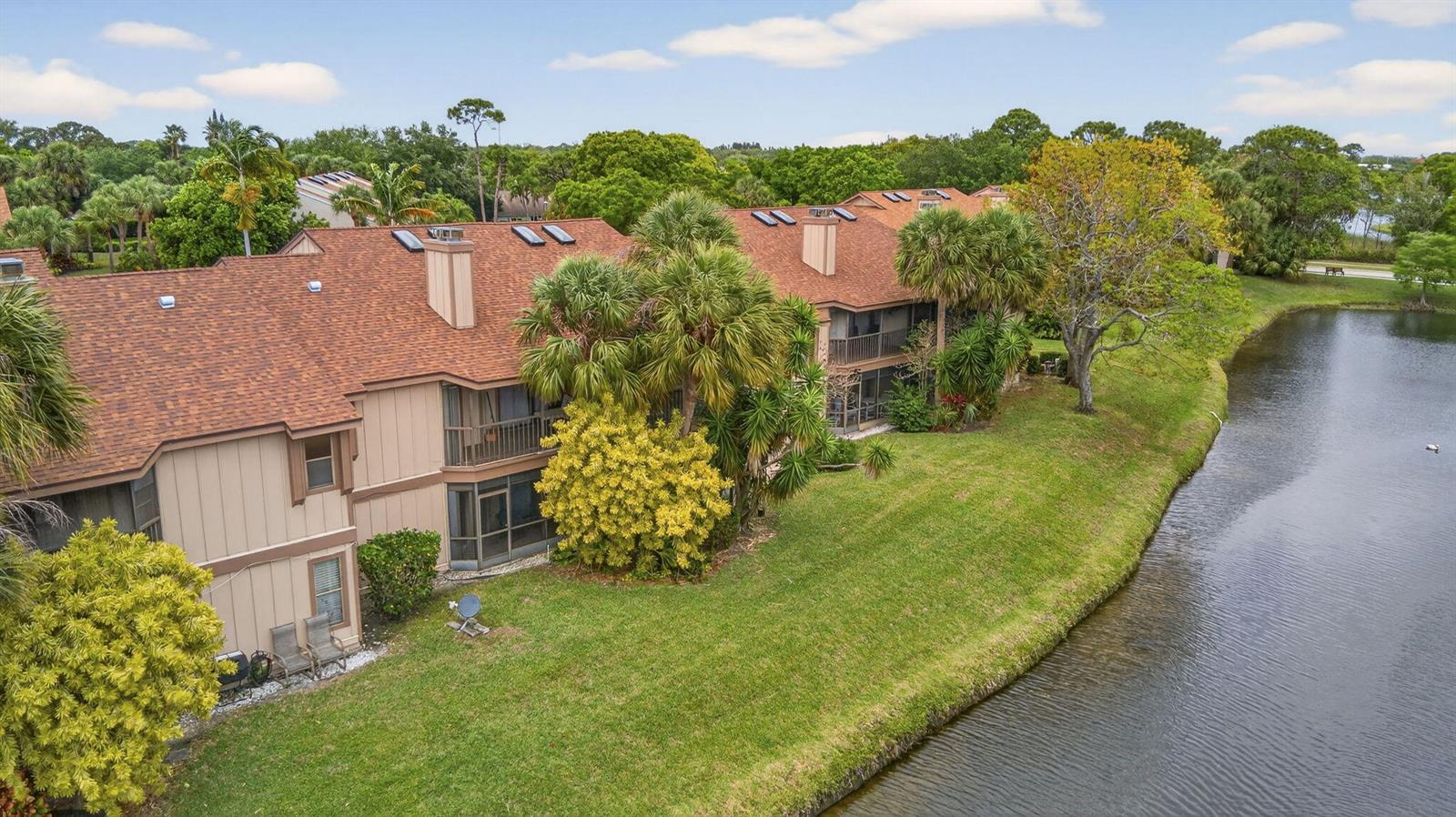 An aerial view shows multi-story residential buildings with brown shingled roofs beside a pond — 500 Crosswinds Drive # C1, FL 33413, FL