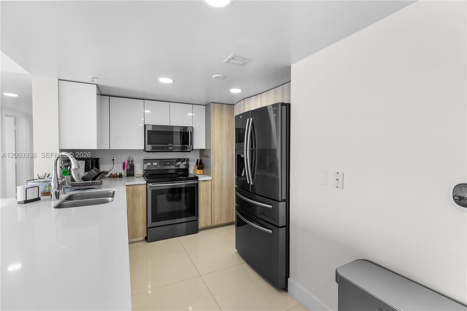 A modern kitchen features white upper cabinets, wood-tone lower cabinets, and black stainless steel appliances — 3000 Coral Way # 1110, Miami FL 33145, MIAMI, FL
