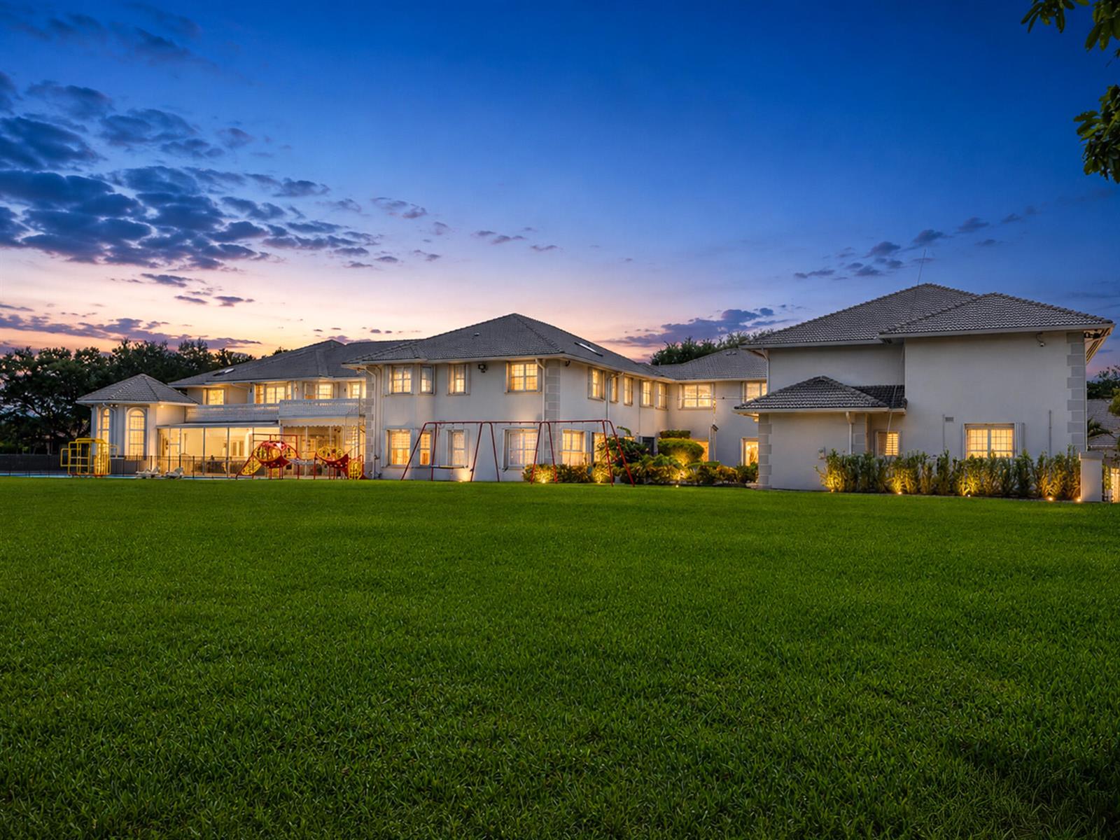 A large two-story house with a sprawling lawn and a playground at dusk — 1800 Eagle Trace Boulevard, Coral Springs FL 33071, CORAL SPRINGS, FL
