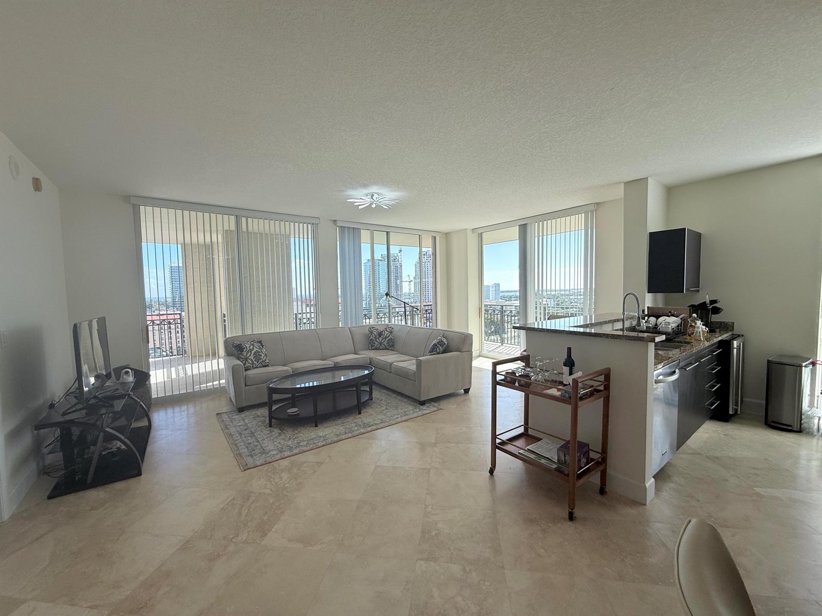 An open-concept living room and kitchen featuring tile floors, a sectional sofa, and balcony views — 550 Okeechobee Boulevard # 1201, West Palm Beach FL 33401, WEST PALM BEACH, FL