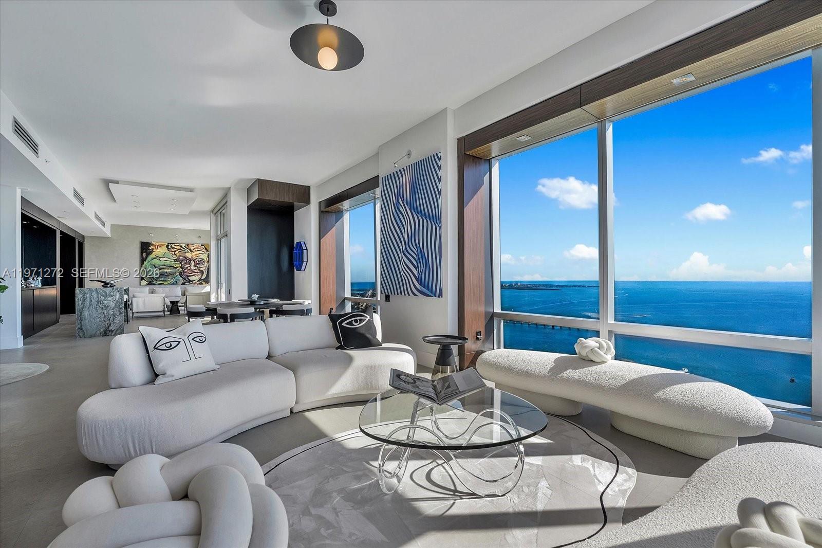 A modern living room features a curved white sofa, glass coffee table, and floor-to-ceiling windows — 1425 Brickell Ave, Miami FL 33131, MIAMI, FL