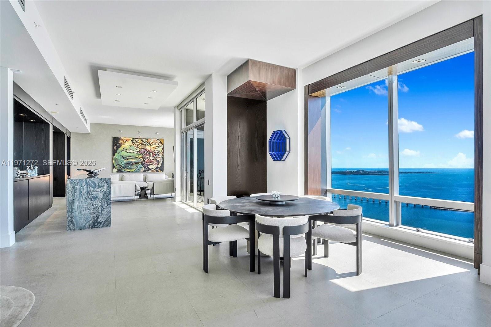 A modern dining area features a round table, upholstered chairs, and floor-to-ceiling ocean views — 1425 Brickell Ave, Miami FL 33131, MIAMI, FL