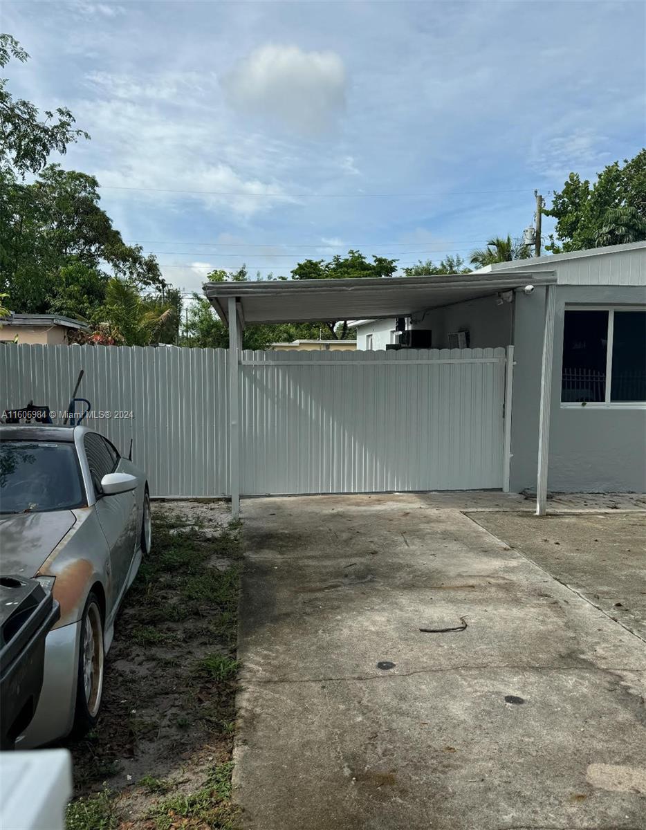 A concrete driveway leads to a white metal gate and carport attached to a house — 110 NW 120 Ter # 0, North Miami FL 33168, NORTH MIAMI, FL