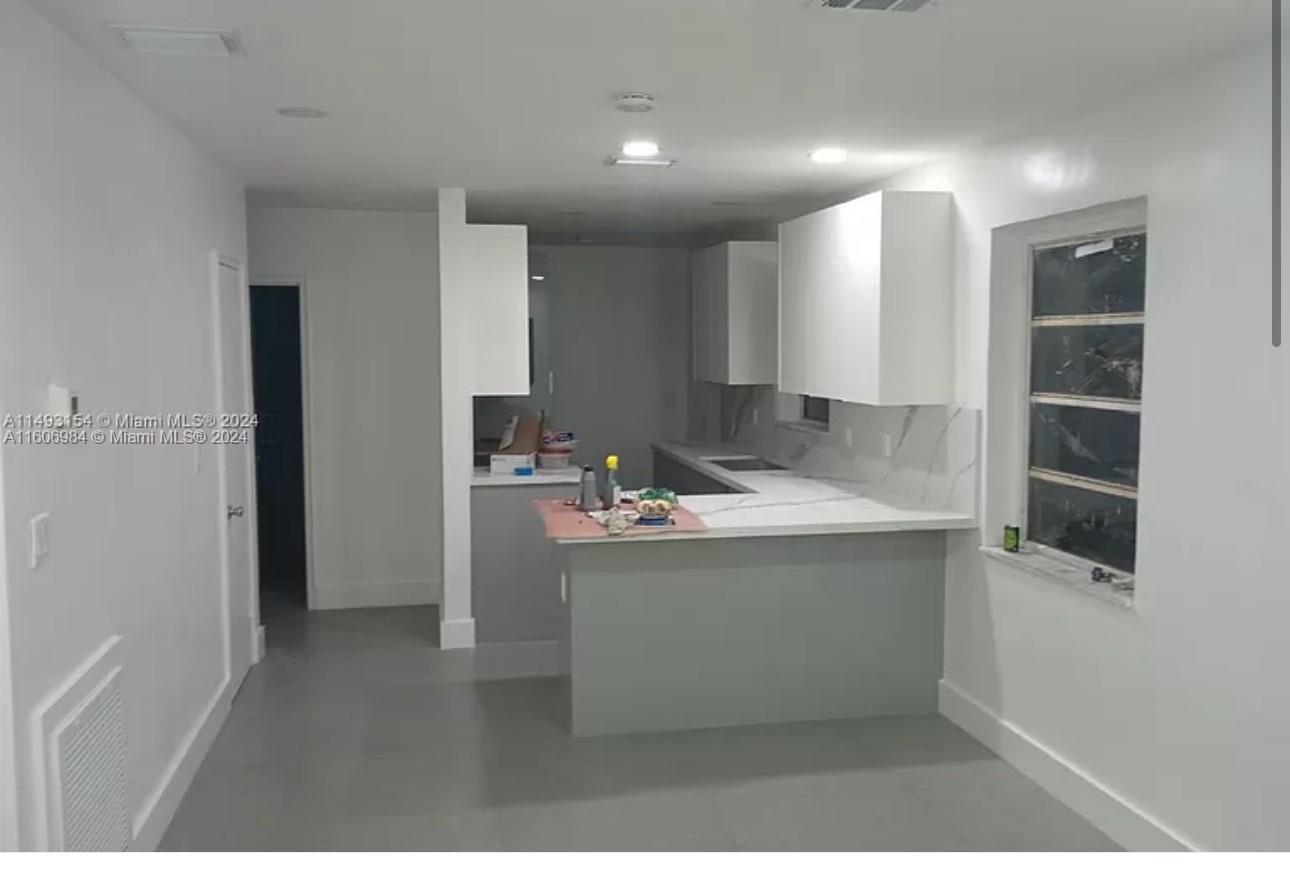 A kitchen features white upper cabinets, grey lower cabinets, and a white countertop peninsula — 110 NW 120 Ter # 0, North Miami FL 33168, NORTH MIAMI, FL