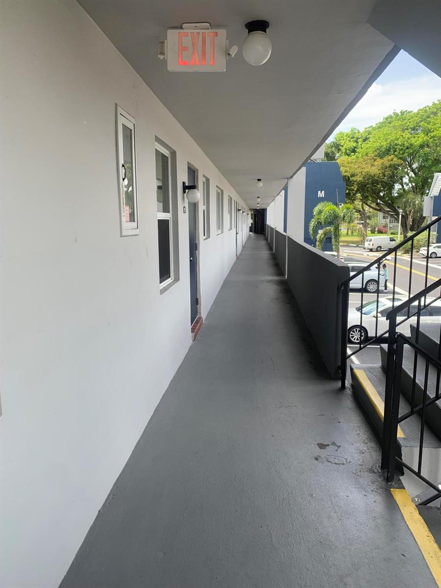An outdoor apartment walkway features gray flooring, white walls, and a metal staircase — 7887 Golf Cir Drive # 212, Margate FL 33063, MARGATE, FL