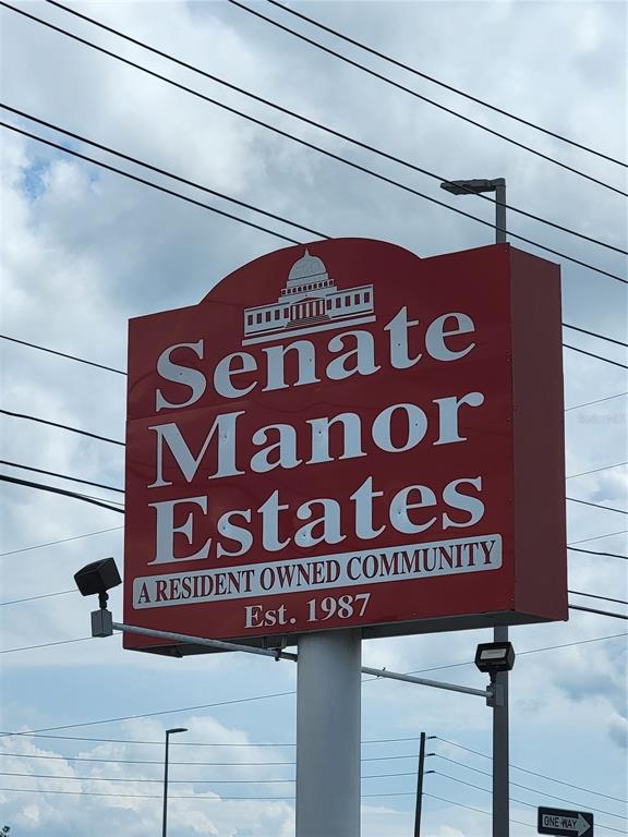 A red sign for Senate Manor Estates stands on a pole against a cloudy sky — 10932 UNION DRIVE, PORT RICHEY, FL