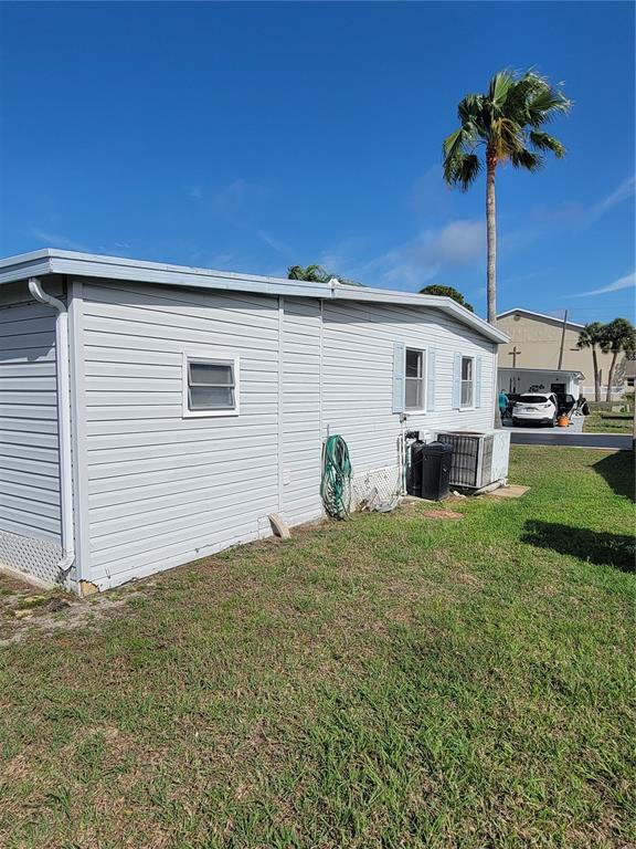 The exterior side of a light gray mobile home features a garden hose and HVAC unit — 10932 UNION DRIVE, PORT RICHEY, FL