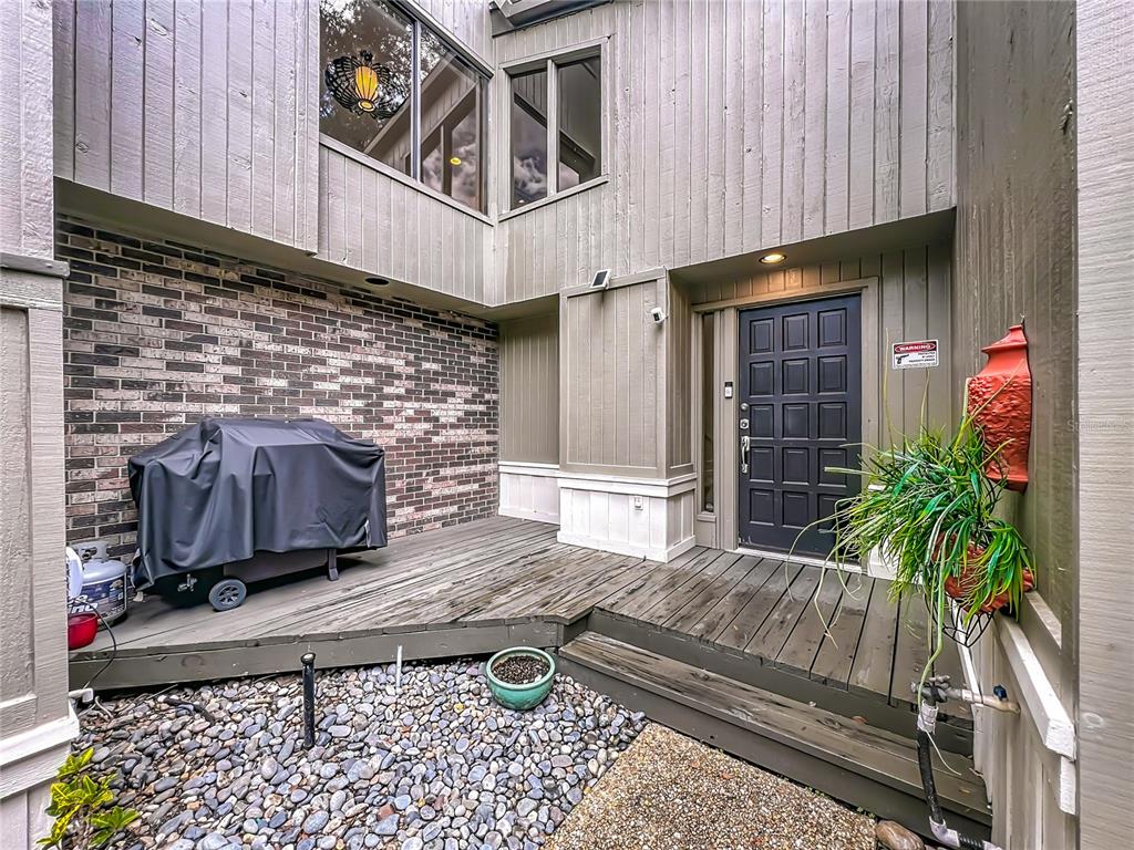 An exterior view of a house entrance with a wooden deck, brick wall, and grill — 542 S OSCEOLA AVENUE UNIT 34, ORLANDO, FL