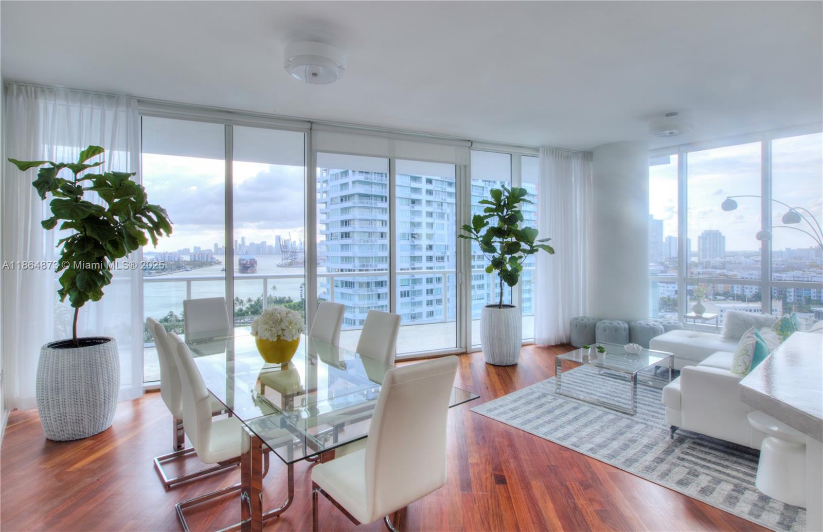 A modern dining and living area with floor-to-ceiling windows, hardwood floors, and city water views — 100 S Pointe Dr # 1501, Miami Beach FL 33139, MIAMI BEACH, FL