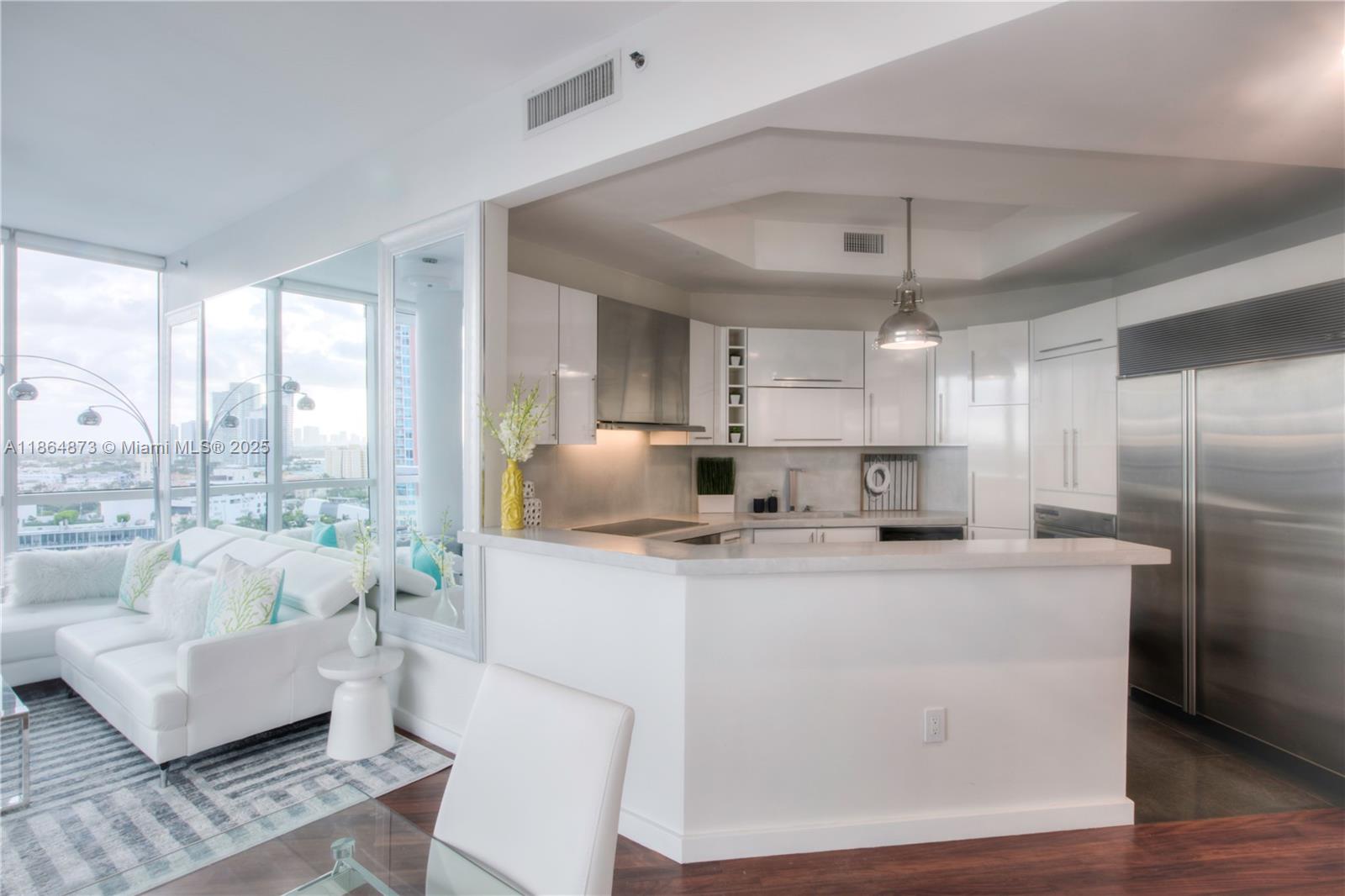 A modern kitchen with white cabinetry and stainless steel appliances overlooks a bright living area — 100 S Pointe Dr # 1501, Miami Beach FL 33139, MIAMI BEACH, FL