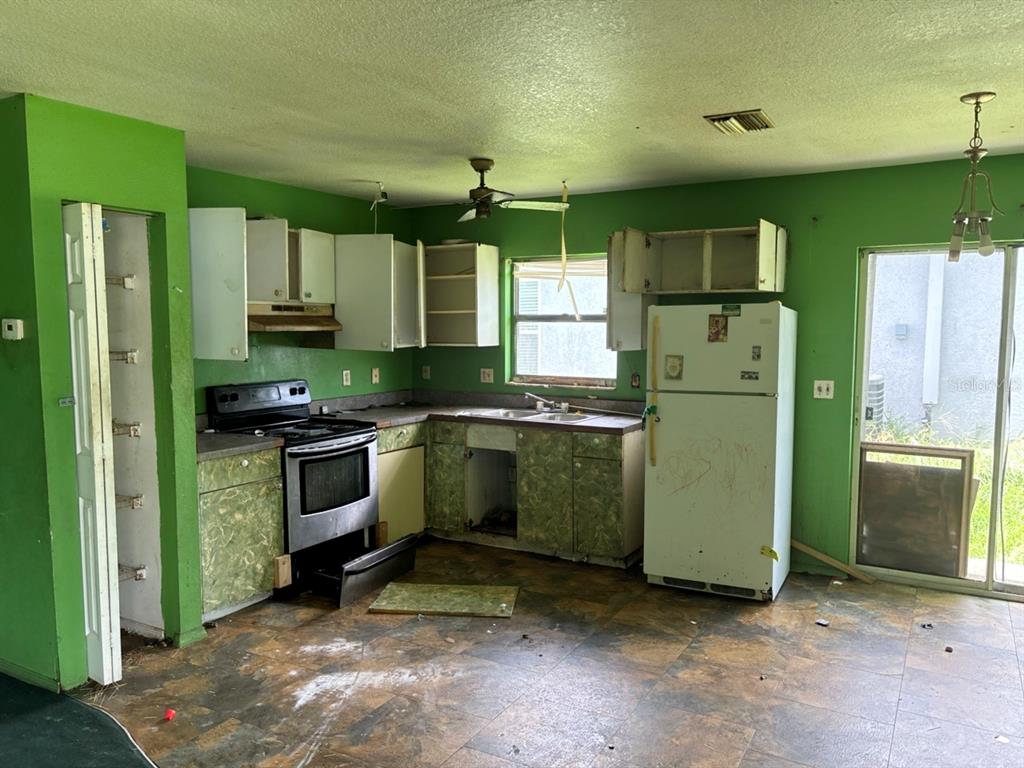 A kitchen with green walls, white cabinets, a stainless steel stove, and dark floor tiles — 2703 1ST AVENUE E, PALMETTO, FL