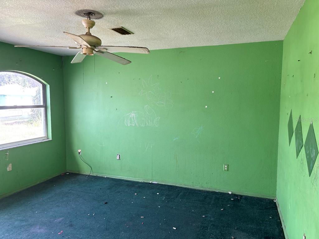 A bedroom with green walls, dark green carpet, a ceiling fan, and a window — 2703 1ST AVENUE E, PALMETTO, FL